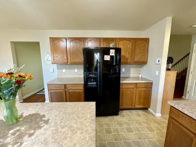 kitchen featuring baseboards, light countertops, decorative backsplash, brown cabinets, and black refrigerator with ice dispenser