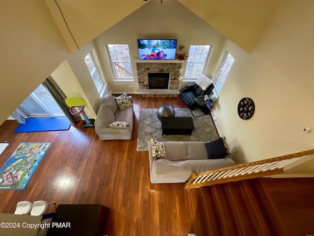 living area featuring high vaulted ceiling, a stone fireplace, and wood finished floors