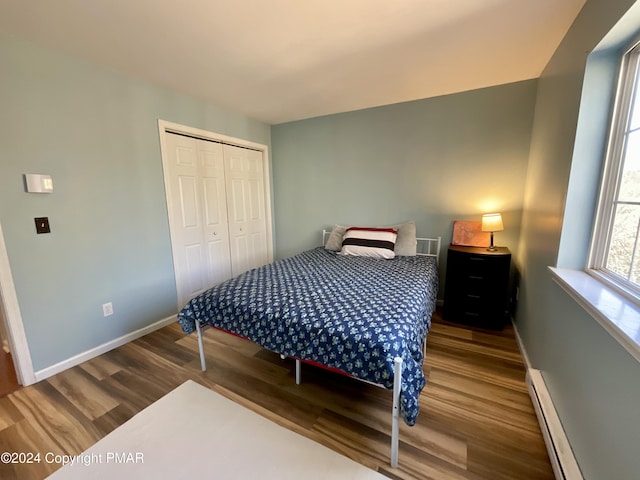 bedroom with a closet, baseboards, baseboard heating, and wood finished floors