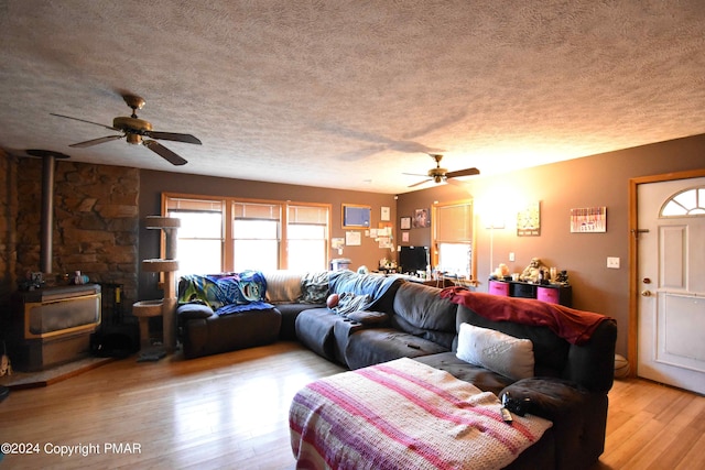 living room featuring ceiling fan, a textured ceiling, wood finished floors, and a wood stove