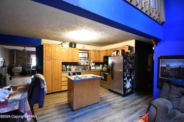 kitchen with a kitchen island, wood finished floors, a wood stove, and stainless steel fridge with ice dispenser