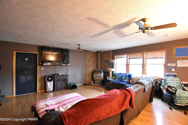 living area with a wood stove, ceiling fan, a textured ceiling, and wood finished floors