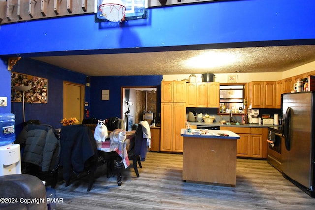 kitchen featuring a textured ceiling, wood finished floors, a kitchen island, and freestanding refrigerator