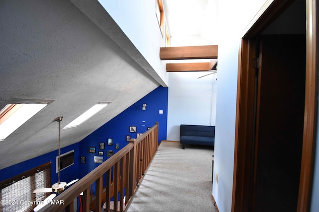 hall featuring carpet, vaulted ceiling with skylight, and a textured ceiling