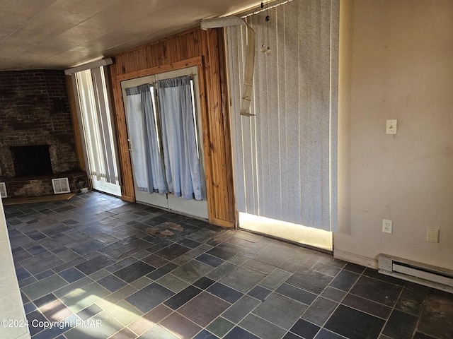 unfurnished living room with baseboard heating, stone finish floor, a brick fireplace, and wooden walls