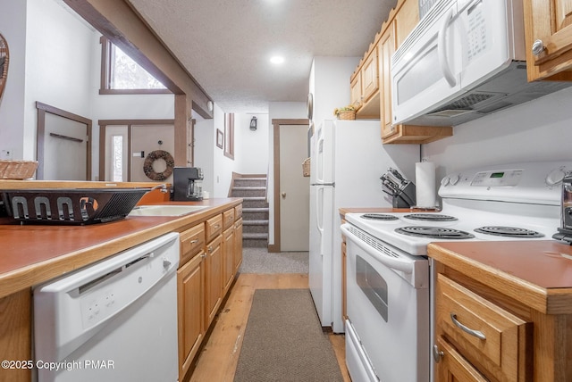 kitchen with a textured ceiling, light countertops, white appliances, and a sink