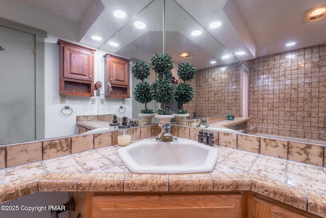 kitchen featuring tile counters, brown cabinets, a sink, and recessed lighting