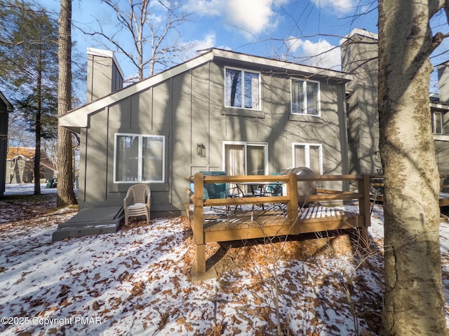 snow covered house featuring a chimney and a deck