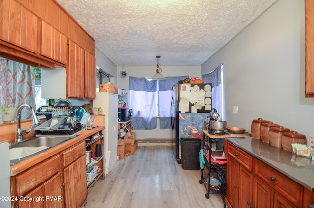 kitchen with a sink, a textured ceiling, freestanding refrigerator, light wood-style floors, and hanging light fixtures