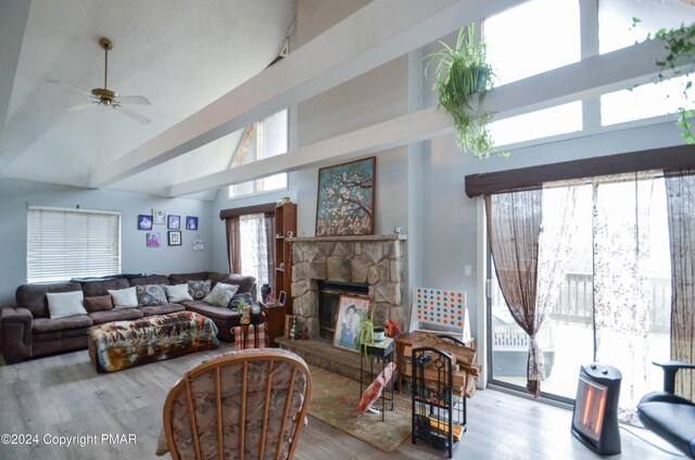 living room featuring ceiling fan, a stone fireplace, high vaulted ceiling, and light hardwood / wood-style floors