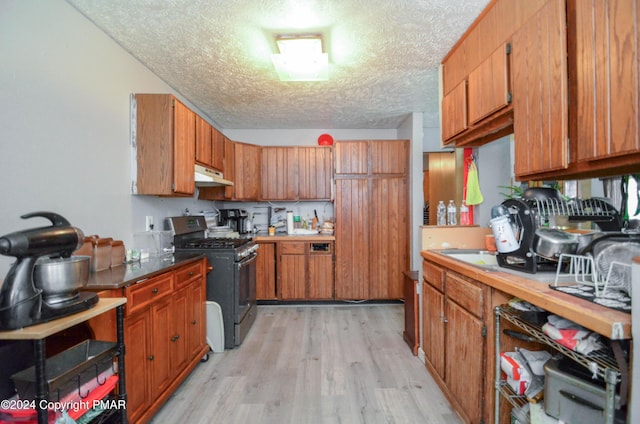 kitchen with stainless steel gas stove, under cabinet range hood, a textured ceiling, brown cabinetry, and light wood finished floors