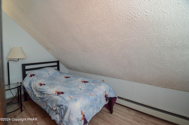 bedroom with a baseboard radiator, a textured ceiling, wood finished floors, and vaulted ceiling