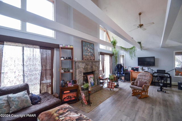 living area featuring a stone fireplace, high vaulted ceiling, ceiling fan, and wood finished floors