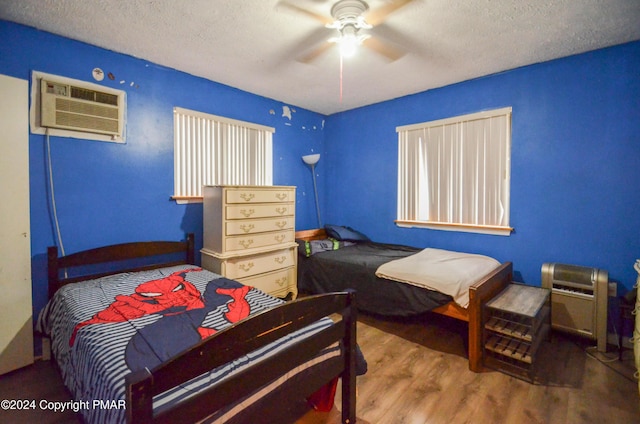 bedroom with ceiling fan, an AC wall unit, wood finished floors, and a textured ceiling