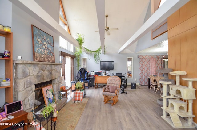 living room with a wealth of natural light, a stone fireplace, wood finished floors, and a ceiling fan