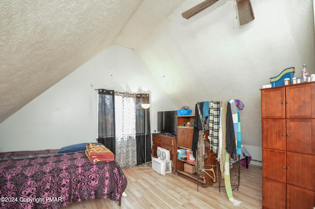 bedroom featuring a ceiling fan, vaulted ceiling, a textured ceiling, a baseboard heating unit, and light wood-type flooring