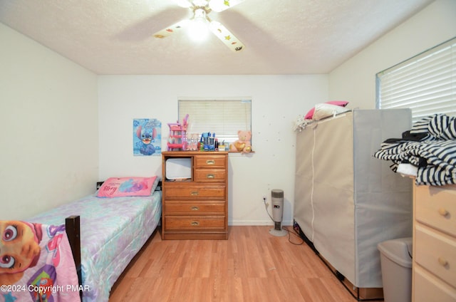 bedroom featuring light wood-type flooring, freestanding refrigerator, and a textured ceiling