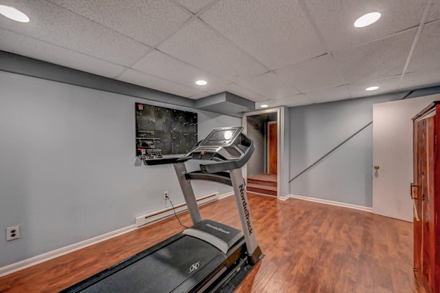 exercise room featuring baseboards, a baseboard heating unit, a drop ceiling, and wood finished floors