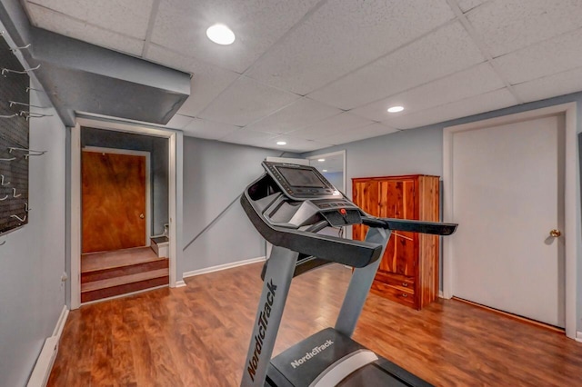 workout area featuring a paneled ceiling, baseboards, and wood finished floors
