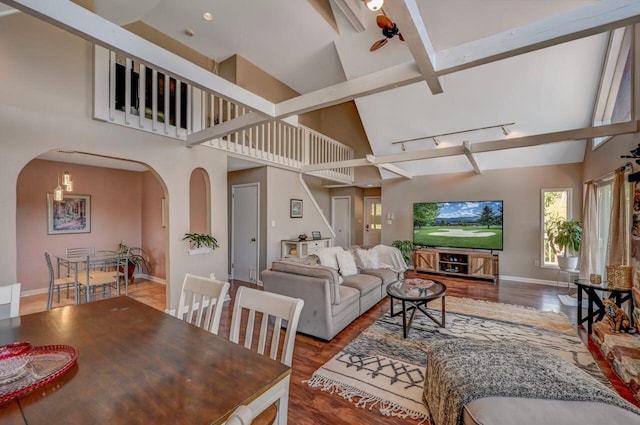 living room featuring beam ceiling, arched walkways, high vaulted ceiling, baseboards, and wood finished floors