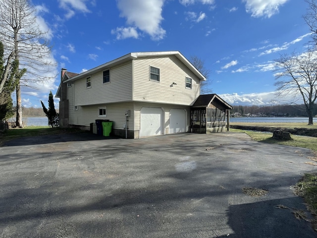 view of side of home featuring a chimney, an attached garage, driveway, and a water view