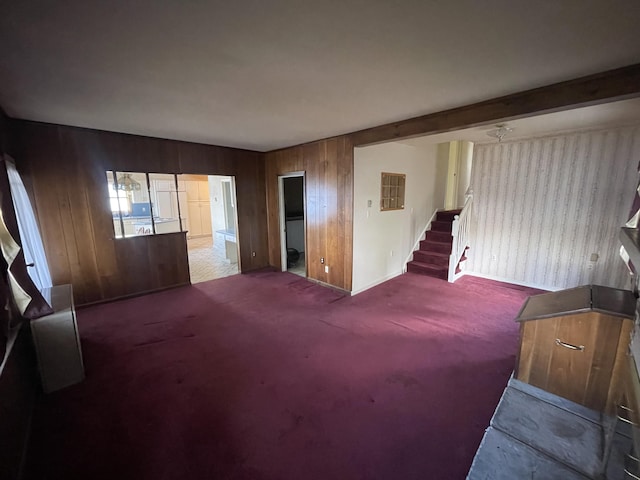 carpeted living area featuring stairway, wood walls, and baseboards