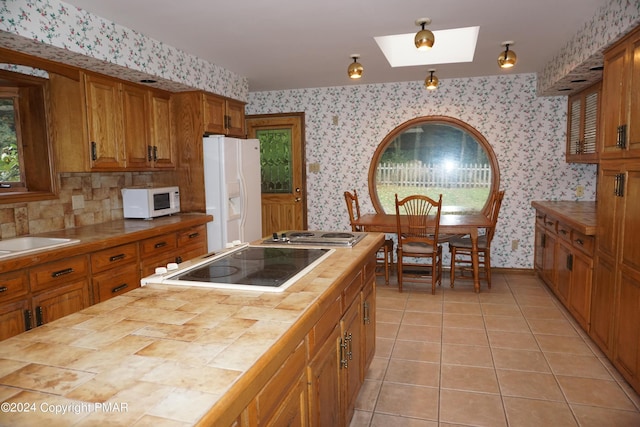 6760 Bear Creek Blvd, Bear Creek Township, PA 18702 - kitchen with wallpapered walls, brown cabinetry, white appliances, tile counters, and a skylight