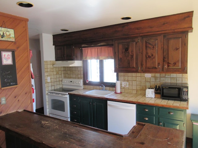 kitchen featuring tasteful backsplash, under cabinet range hood, tile countertops, white appliances, and a sink