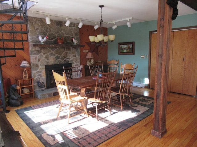 dining room featuring hardwood / wood-style floors, a stone fireplace, baseboard heating, and an inviting chandelier