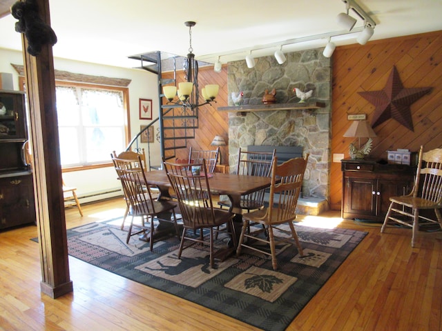 dining space with track lighting, wood walls, wood-type flooring, a baseboard heating unit, and a notable chandelier