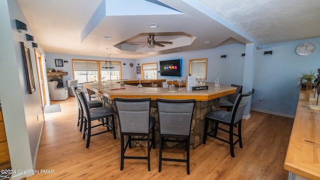 dining area with a ceiling fan, a tray ceiling, light wood-style flooring, and baseboards