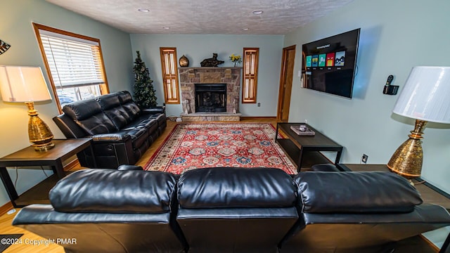 living room with a textured ceiling, a stone fireplace, wood finished floors, and baseboards