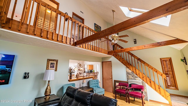 living area with a skylight, ceiling fan, stairway, high vaulted ceiling, and beam ceiling