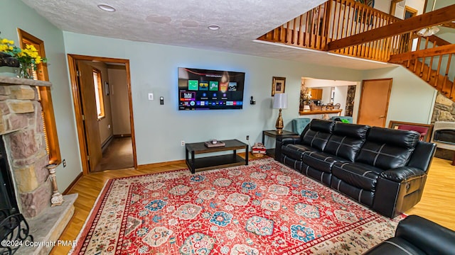 living room with heating unit, a stone fireplace, light hardwood / wood-style floors, and a textured ceiling