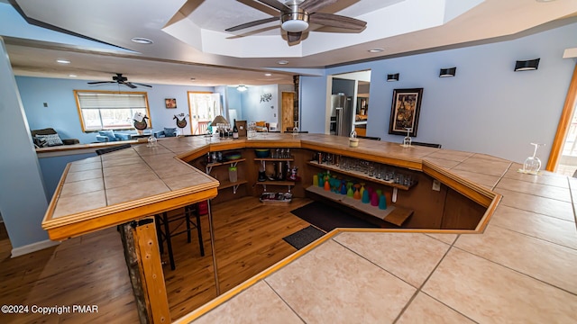 kitchen with a raised ceiling, tile countertops, wood finished floors, stainless steel refrigerator with ice dispenser, and recessed lighting