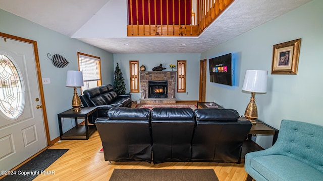 living area featuring high vaulted ceiling, a stone fireplace, wood finished floors, and baseboards