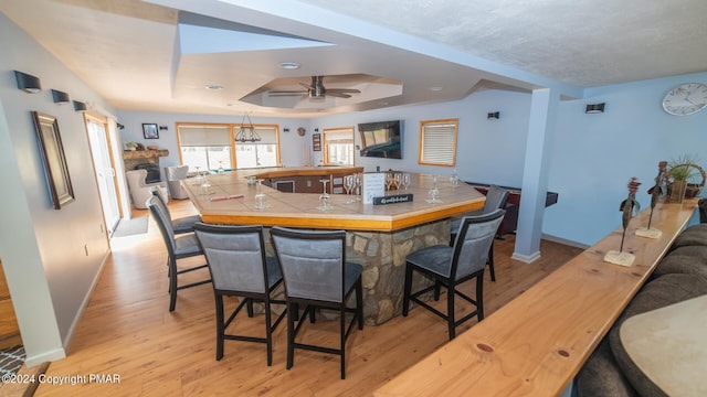 kitchen featuring light wood-style floors, a tray ceiling, a breakfast bar, and baseboards