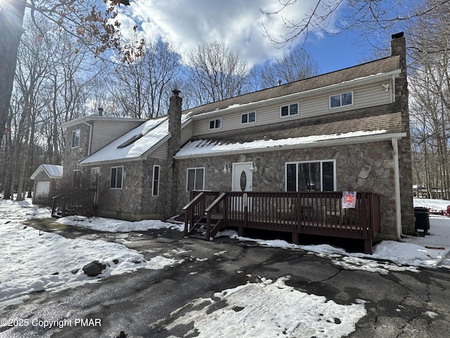 view of front facade featuring stone siding, a chimney, and a wooden deck