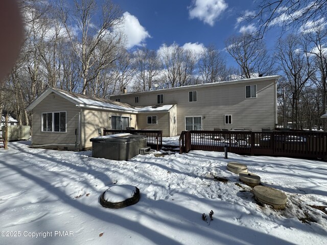 snow covered back of property featuring a hot tub and a wooden deck