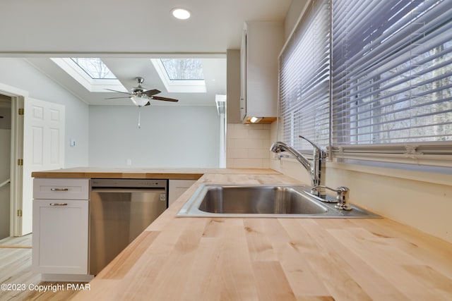 kitchen with butcher block counters, backsplash, stainless steel dishwasher, white cabinetry, and a sink