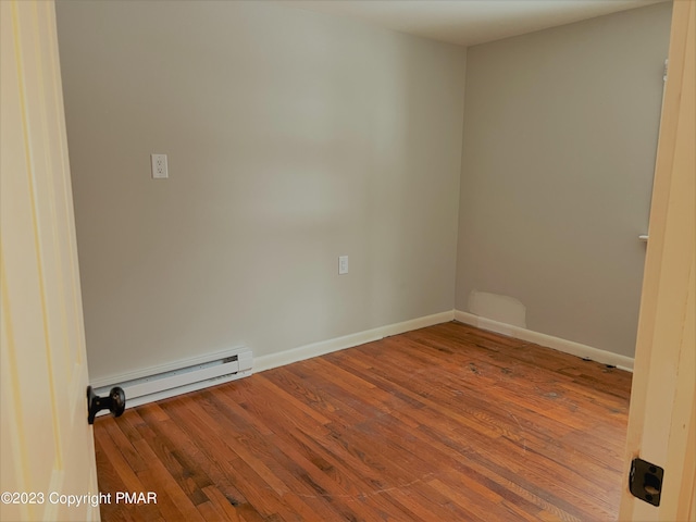 empty room featuring baseboards, a baseboard heating unit, and wood finished floors