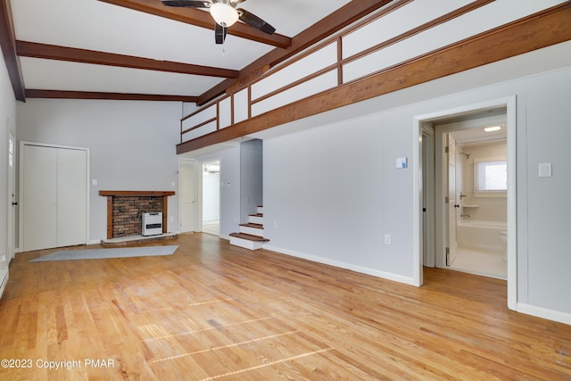 unfurnished living room with beam ceiling, a fireplace, stairway, light wood-style flooring, and a ceiling fan