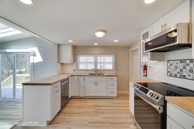 kitchen featuring appliances with stainless steel finishes, white cabinetry, light wood-style flooring, and wood counters