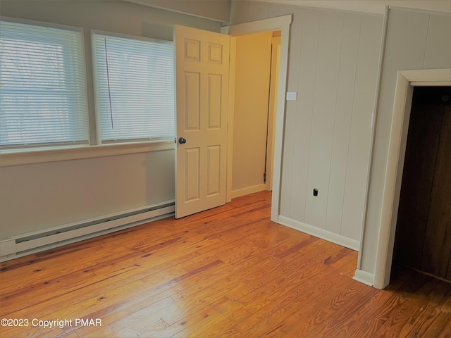 unfurnished bedroom featuring light wood finished floors, a baseboard radiator, and baseboards