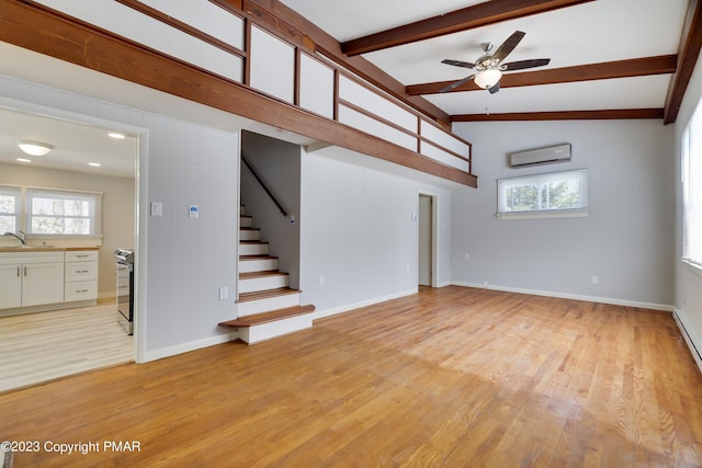 empty room with a wall unit AC, a sink, a healthy amount of sunlight, stairs, and light wood-style floors