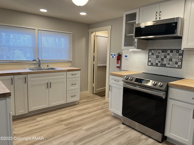 kitchen with a sink, wooden counters, appliances with stainless steel finishes, light wood finished floors, and glass insert cabinets