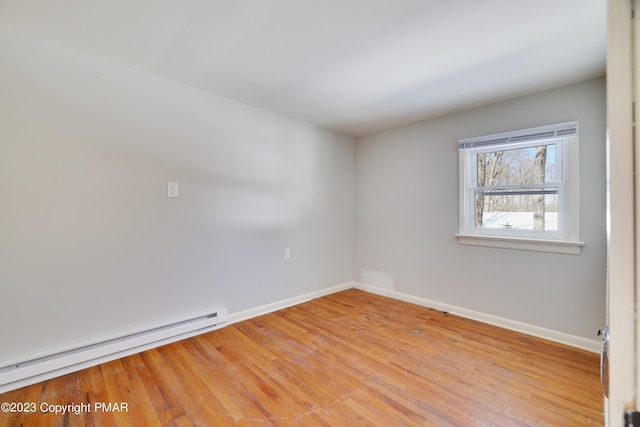 spare room with a baseboard heating unit, light wood-type flooring, and baseboards