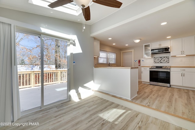 kitchen with stainless steel electric range oven, light wood finished floors, decorative backsplash, white cabinets, and exhaust hood