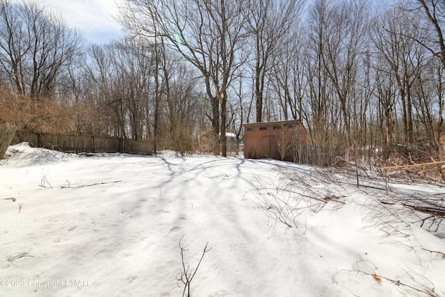 yard covered in snow with an outdoor structure, fence, and a storage unit