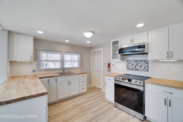 kitchen with appliances with stainless steel finishes, butcher block counters, white cabinetry, and a sink